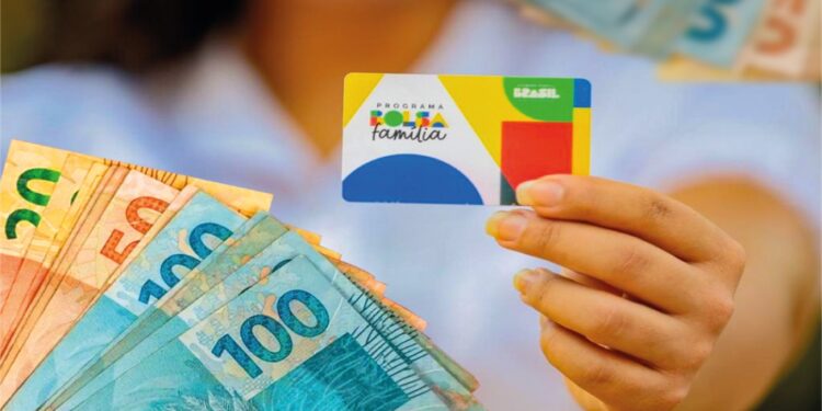 Pessoa segurando o cartão do Bolsa Família com dinheiro em notas ao fundo
